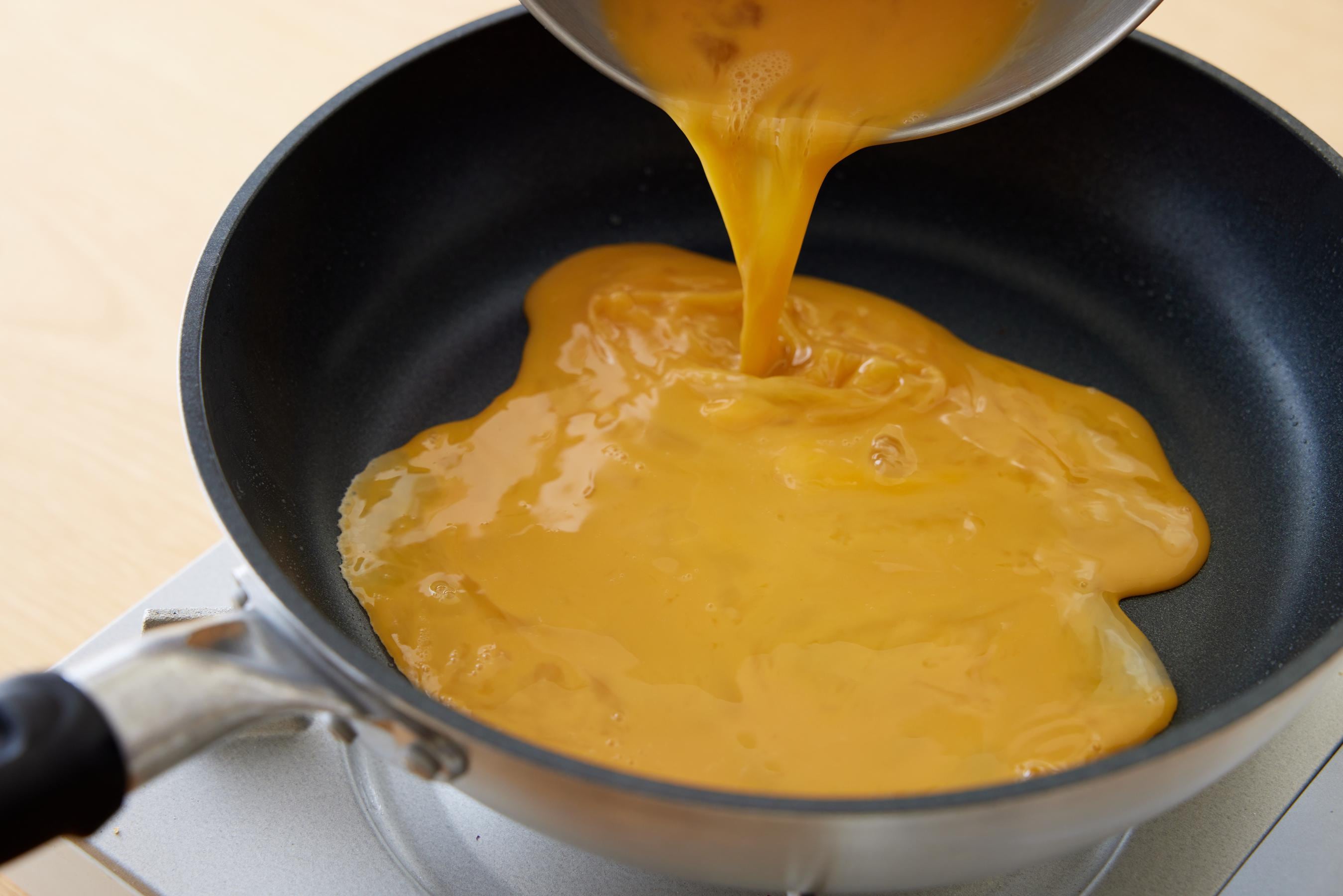 Pour the beaten egg mixture into the fry pan.